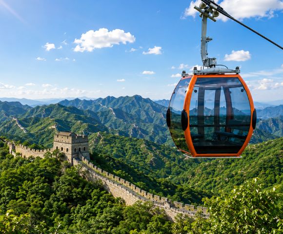 An orange and glass cable car gondola hangs suspended in the foreground against a backdrop of the Great Wall of China snaking across lush, green, mountainous terrain under a blue sky with scattered clouds.