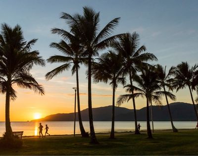 Silhouetted palm trees line a beach at sunset with two figures jogging along the water's edge.