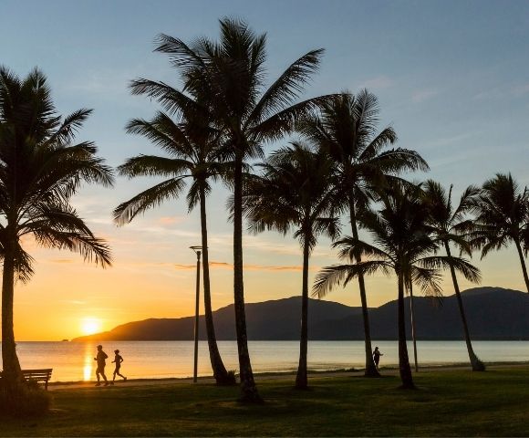 Silhouetted palm trees line a beach at sunset with two figures jogging along the water's edge.