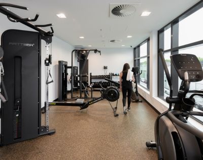 A woman walks through a bright modern gym lined with strength machines and cardio equipment, creating a clean, focused workout atmosphere.