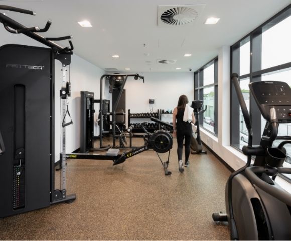 A woman walks through a bright modern gym lined with strength machines and cardio equipment, creating a clean, focused workout atmosphere.