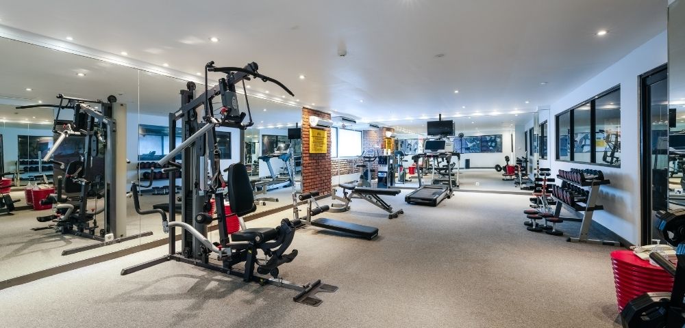 A well-equipped gym with cardio machines, weight machines, dumbbells, and benches.