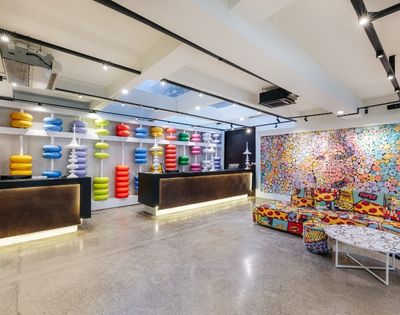 A brightly colored, eclectic reception area with two dark reception desks, one displaying shelves of colorful, stackable abacus-like sculptures and the other against a wall covered by a vibrant, pop-art-style mural.