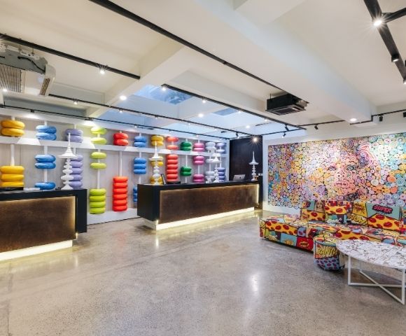 A brightly colored, eclectic reception area with two dark reception desks, one displaying shelves of colorful, stackable abacus-like sculptures and the other against a wall covered by a vibrant, pop-art-style mural.