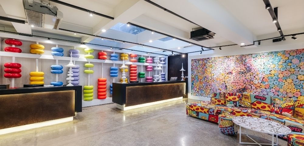 A brightly colored, eclectic reception area with two dark reception desks, one displaying shelves of colorful, stackable abacus-like sculptures and the other against a wall covered by a vibrant, pop-art-style mural.