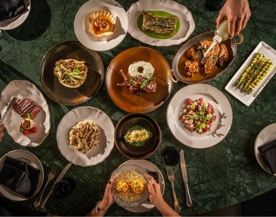 Overhead view of a dark green dining table set with colorful gourmet dishes as guests serve food, creating an elegant, convivial mood.