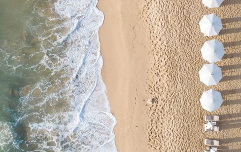 Aerial view of a sunny beach filled with colourful umbrellas and chairs scattered along the sandy shore.