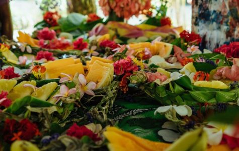 Tropical fruits like papaya and pineapple are artfully arranged among vibrant red and white flowers on lush greenery, conveying a festive and tropical vibe.