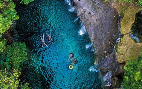 Aerial view of people floating and tubing in a vibrant turquoise natural pool surrounded by lush green forest.
