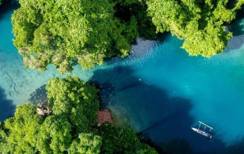 Aerial view of a vibrant blue river winding through a dense, lush green jungle, with two small outrigger canoes navigating the clear water.