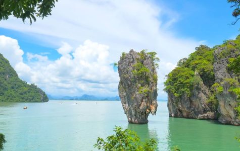 Serene coastal scene in Phang Nga Bay featuring towering limestone islets emerging from tranquil waters against a bright blue sky, framed by lush greenery.