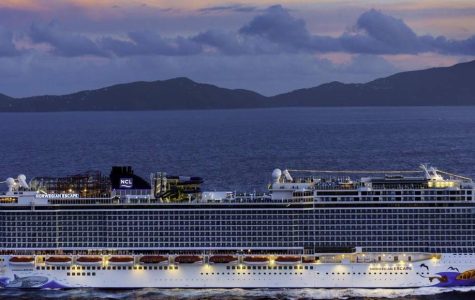 A large cruise ship sails on a calm sea during sunset, with island silhouettes in the background. The sky is a mix of blue and pink hues, creating a serene atmosphere.