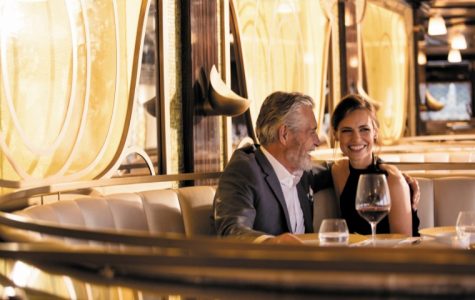 A couple smiles warmly while seated at an upscale restaurant booth. Dim lighting and elegant decor create a romantic and cozy atmosphere.