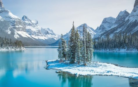 Snow-covered mountains and pine trees surround a tranquil turquoise lake under a clear blue sky, creating a serene and peaceful winter scene.