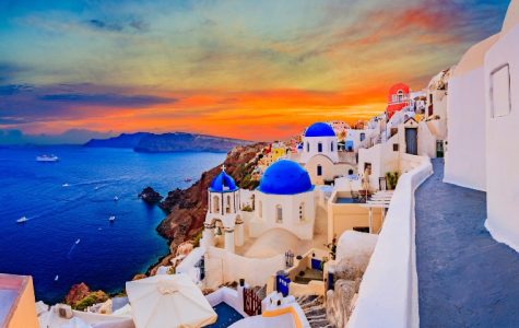 Sunset view of Santorini, Greece, with white buildings and blue domes. The vibrant sky reflects on the sea, evoking a serene, picturesque ambiance.
