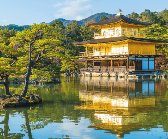 Golden Pavilion temple reflected in a calm pond, surrounded by pine trees and mountainous forest in the background.