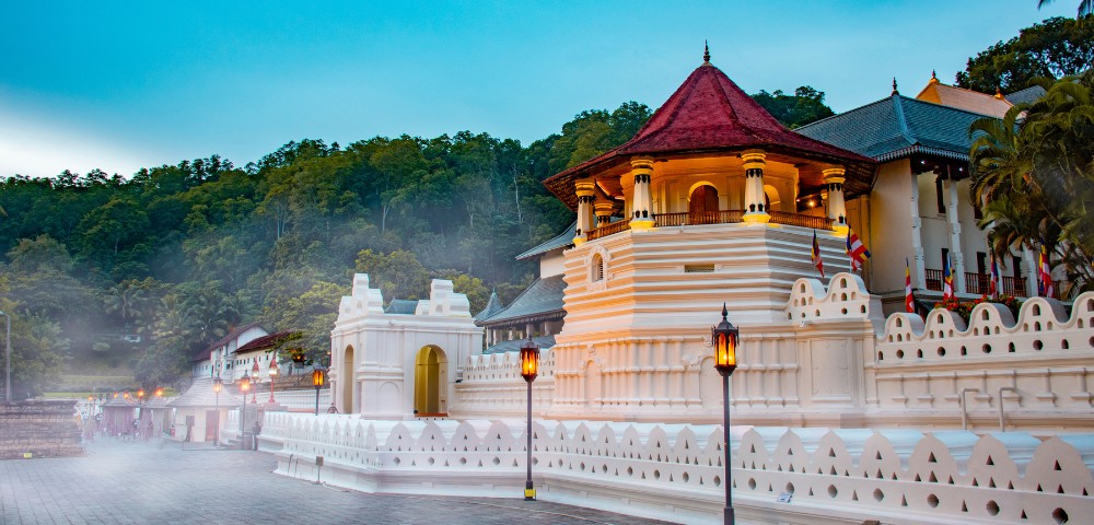 A serene temple complex with white walls and a red-tiled roof, surrounded by mist and lush greenery under a clear blue sky. Peaceful ambiance.