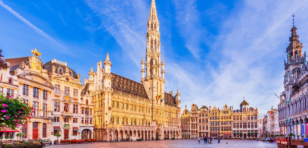 Grand Place in Brussels, featuring ornate, historic buildings with intricate facades. The square is bathed in a warm, golden glow under a clear blue sky.