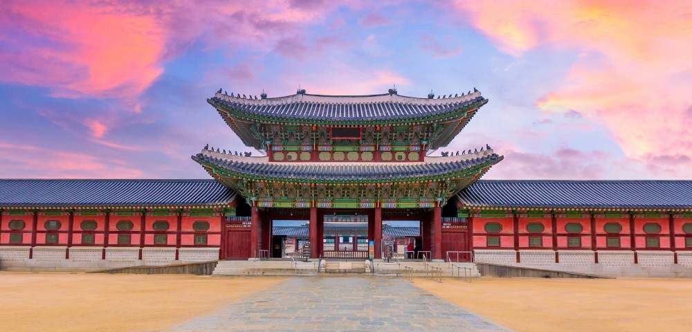 Historic Gyeongbokgung Palace gate with traditional architecture, vibrant colors, under a dramatic pink and purple sky at sunset. Majestic and serene.