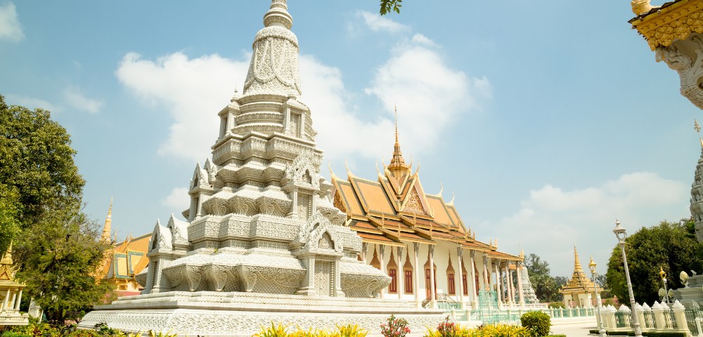 White ornate stupa and temple under a bright blue sky with scattered clouds, surrounded by lush greenery, conveying a peaceful and majestic atmosphere.