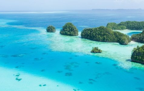 Aerial view of lush green islands surrounded by vibrant, clear blue waters and a sandy beach floor showing through the shallow waters.