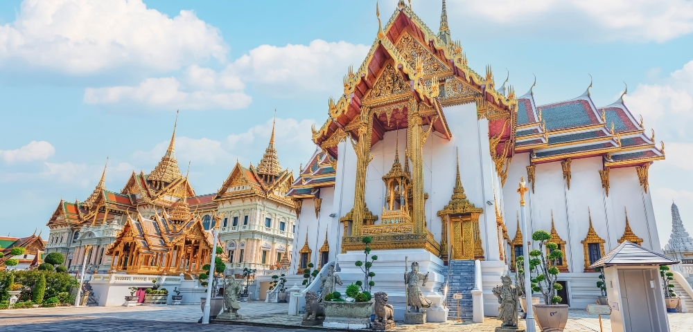 Ornate Thai temple with golden details and intricate architecture under a bright blue sky, conveying serenity and cultural richness.