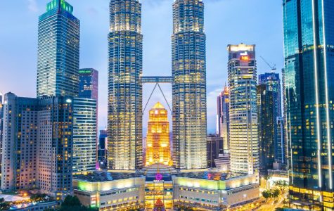 Kuala Lumpur skyline at dusk, featuring the illuminated Petronas Twin Towers surrounded by modern skyscrapers and a foreground of lush green parkland.