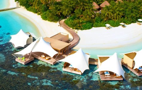 Aerial view of a tropical island with luxurious overwater cabanas on turquoise waters. White sand beach, lush greenery, and a serene, inviting atmosphere.