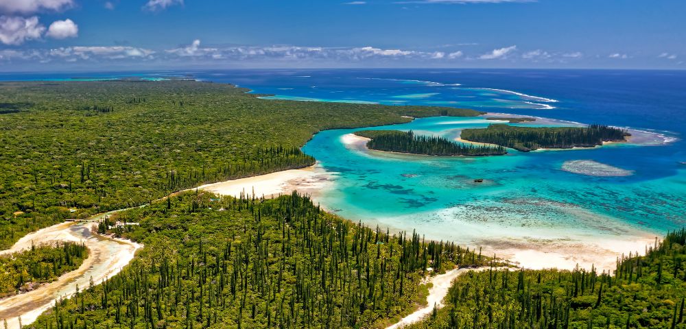 Aerial view of a lush green island surrounded by turquoise waters and coral reefs. Sandy beaches and dense forests create a serene, tropical paradise.