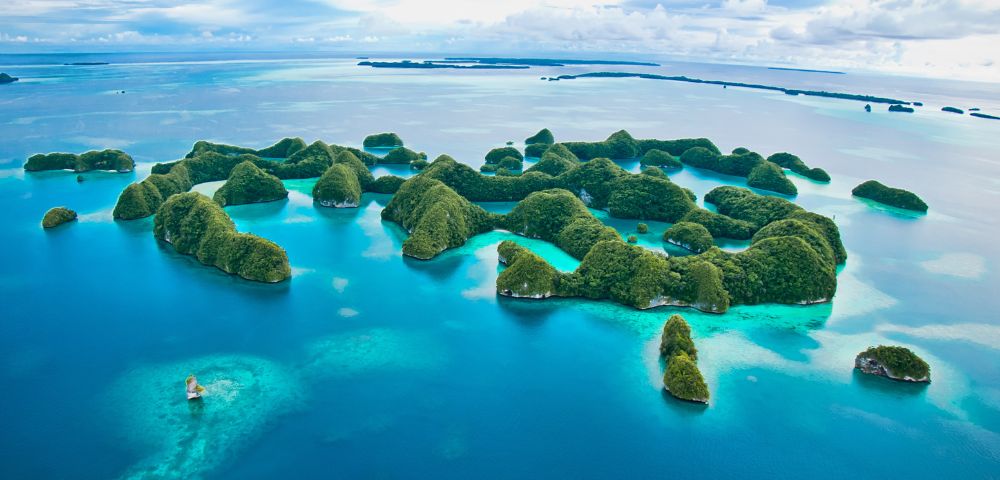 Aerial view of lush, green islands scattered across vibrant turquoise water, under a cloudy sky. The scene conveys a tranquil and tropical paradise.