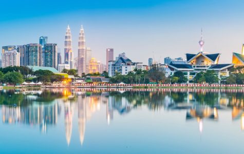 Reflective cityscape of Kuala Lumpur at twilight, featuring the Petronas Twin Towers, a television tower, and modern skyscrapers reflected in a calm lake.